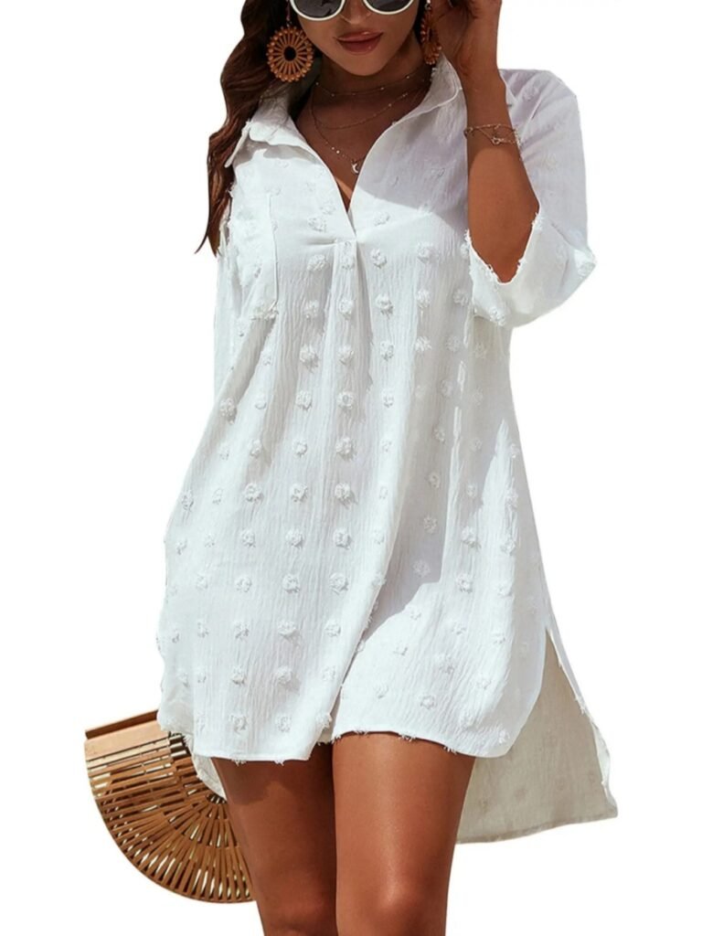 White textured blouse dress with floral pom-pom details, 3/4 sleeves, V-neck, and side slit, worn with sunglasses and woven bag.