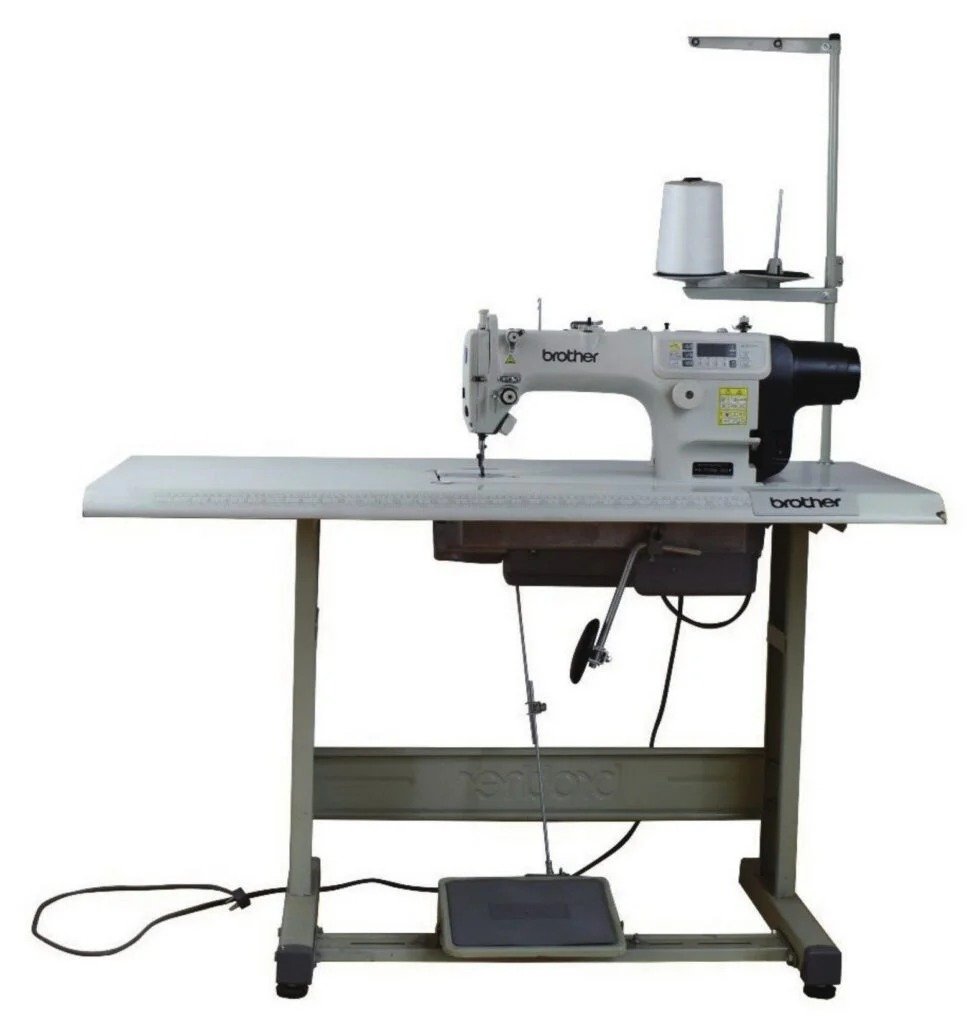 Brother industrial sewing machine on metal worktable with foot pedal, white spool of thread, used for swimwear manufacturer production.