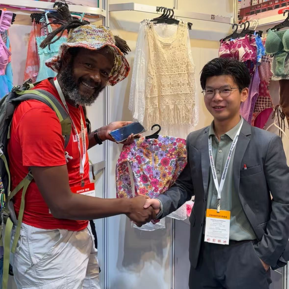 Two men shaking hands at a trade show booth displaying colorful swimwear.