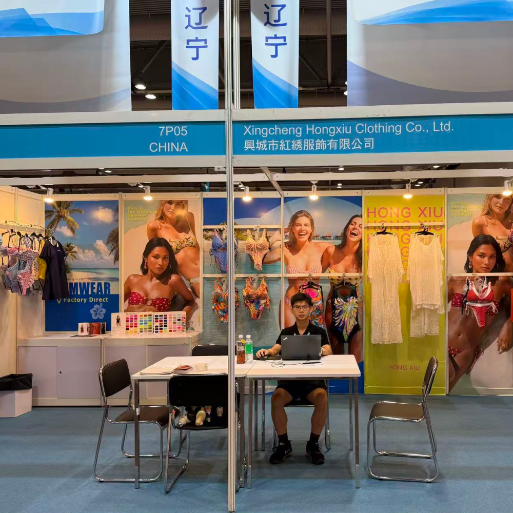 A swimwear manufacturer's trade show booth displaying bikinis, cover-ups, and fabric swatches.