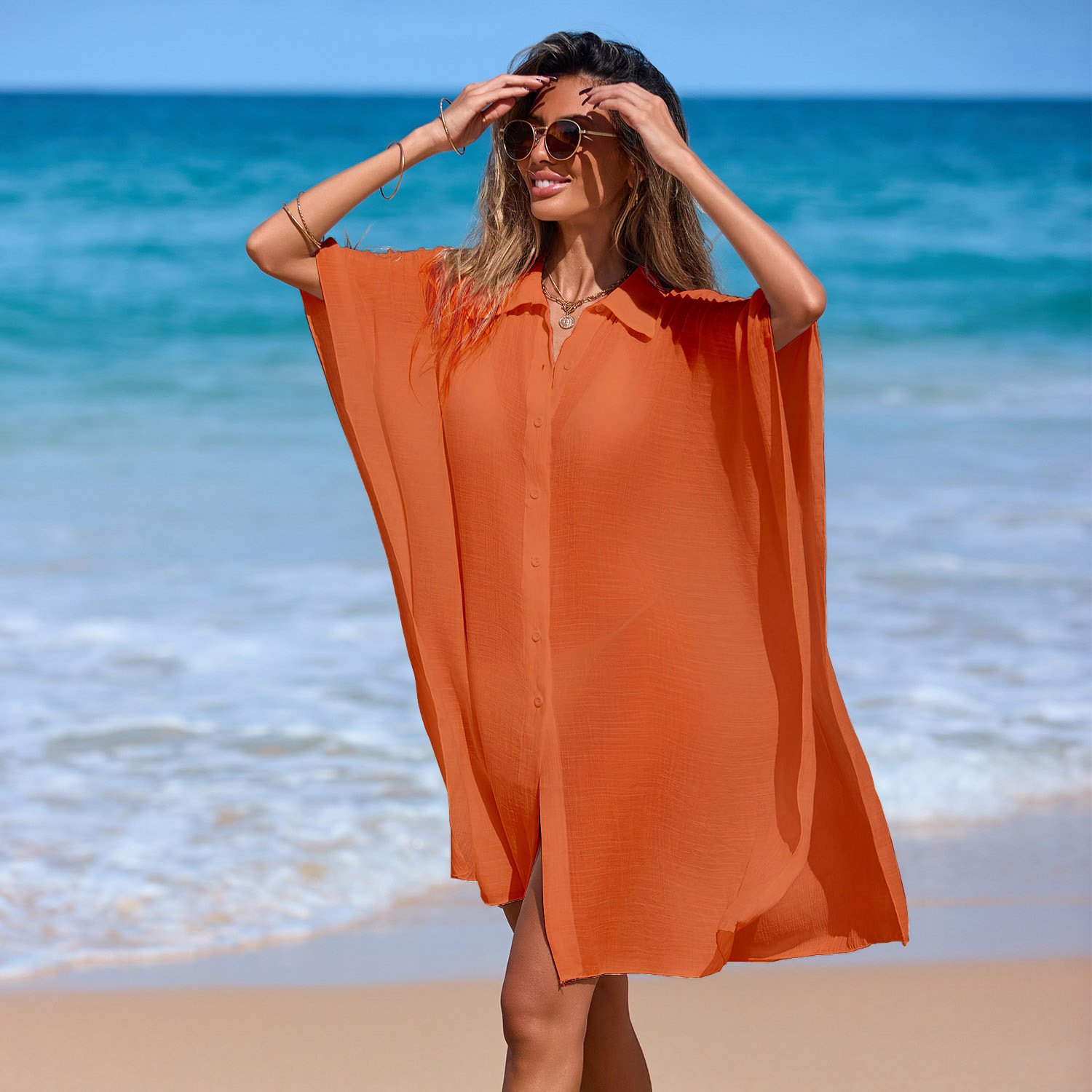 Woman wearing an orange button-front collared kaftan cover-up with wide sleeves on the beach.