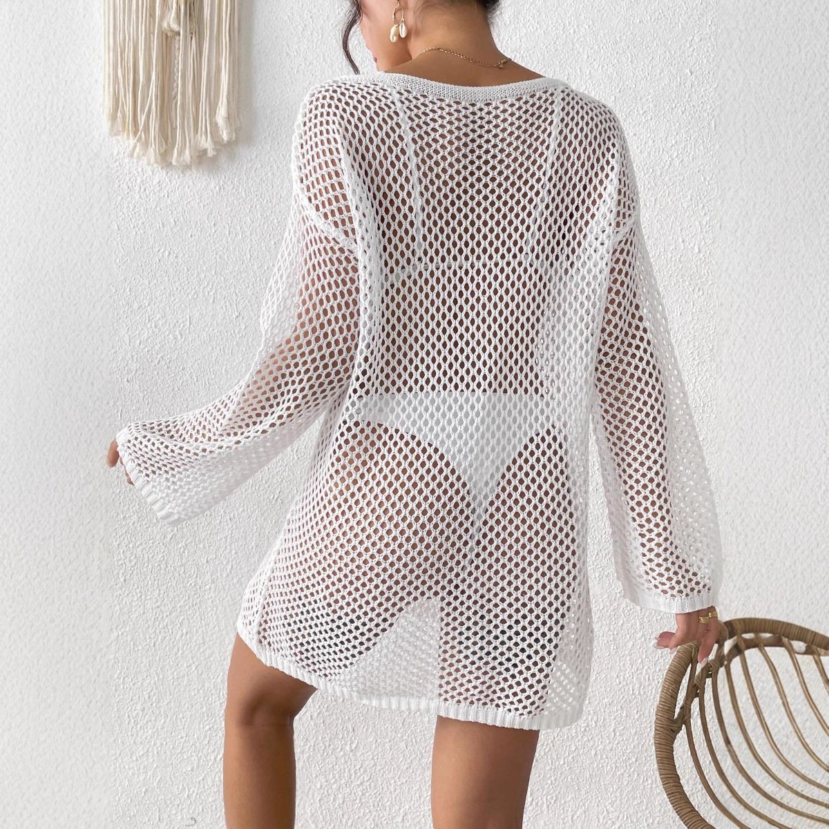 Back view of a woman wearing a white long sleeve open knit tunic cover-up over white bikini bottoms.