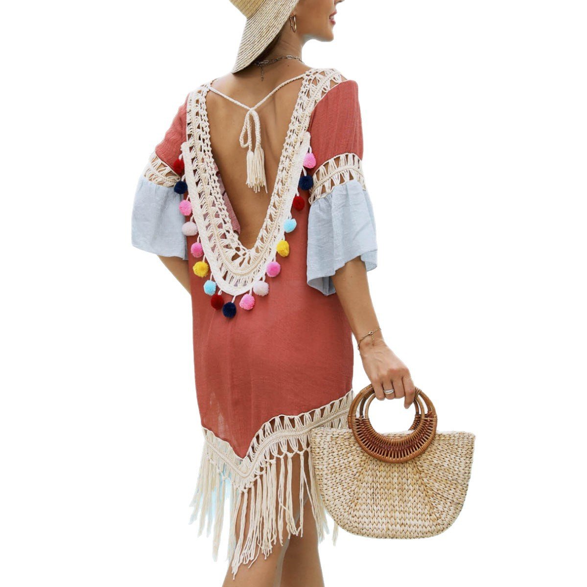 Back view of a woman wearing a dusty rose open-back beach cover-up with white crochet trim, colorful pom-poms,