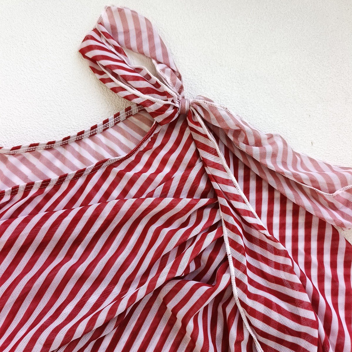 Close-up of a red and white striped long sleeve cover-up featuring an asymmetric shoulder tie and diagonal ruching.