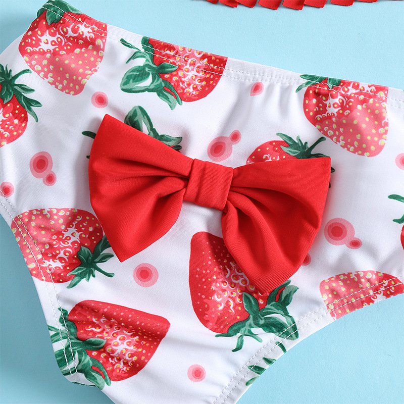 Close-up of girls' white high-waisted bikini bottoms featuring a strawberry print and a large red front bow.