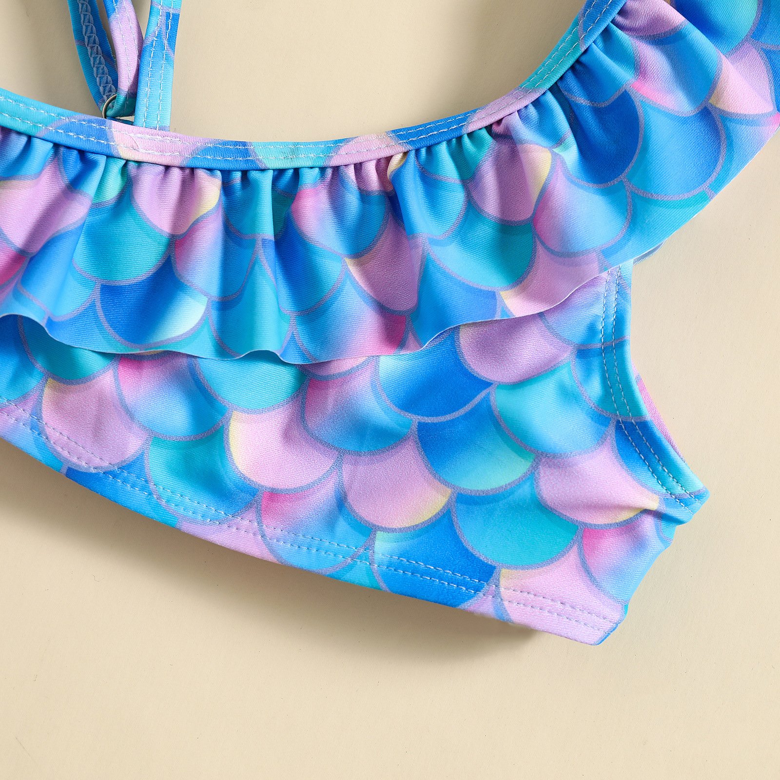 Close-up of a girls' mermaid-scale print bikini top featuring ruffled trim and adjustable straps.