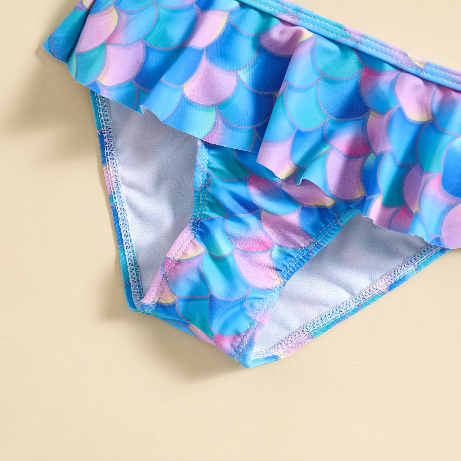 Girls' bikini bottom featuring a colorful mermaid scale print with a ruffled overlay and white lining.