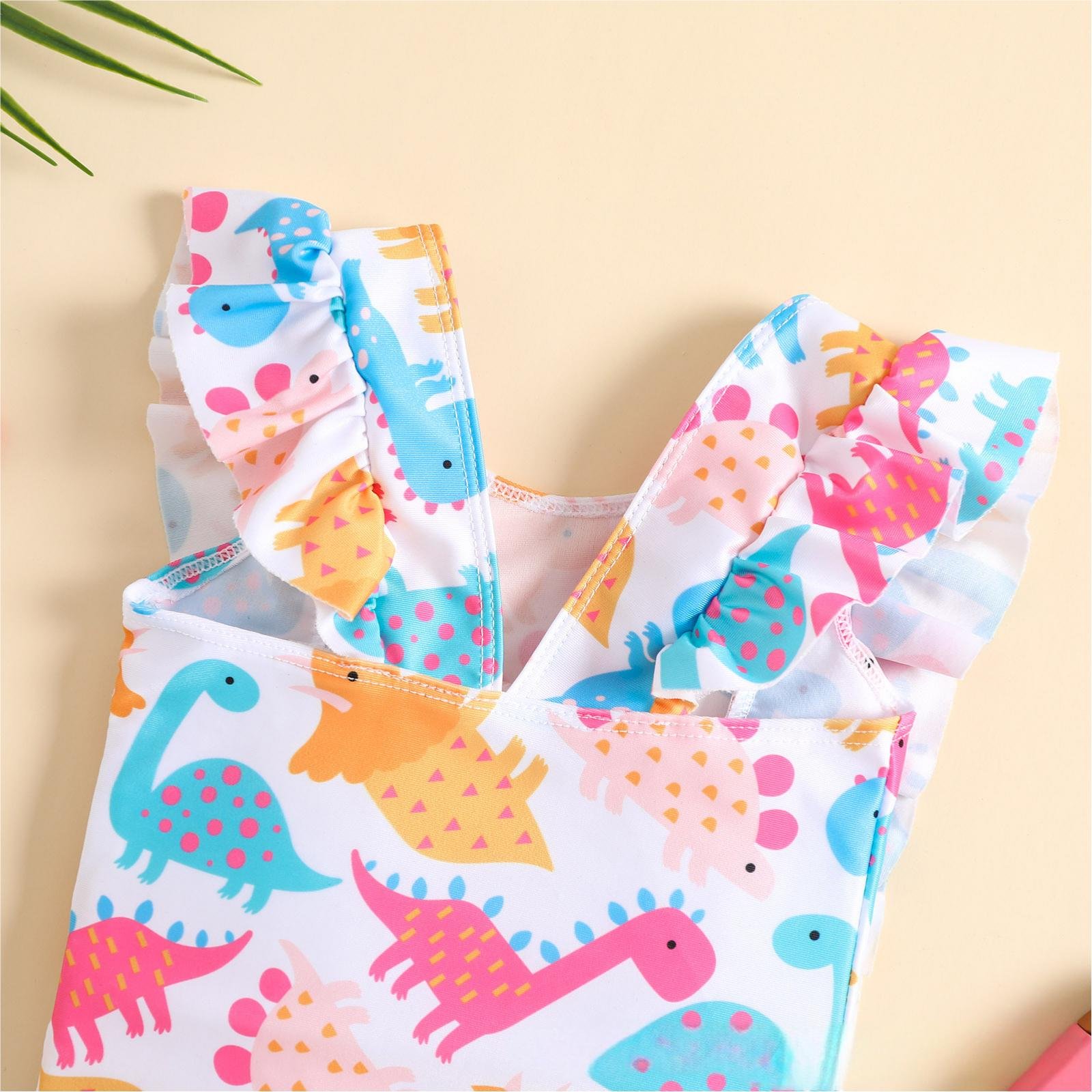 Girls' one-piece swimsuit with dinosaur print, featuring ruffled shoulder straps and a scoop neckline.