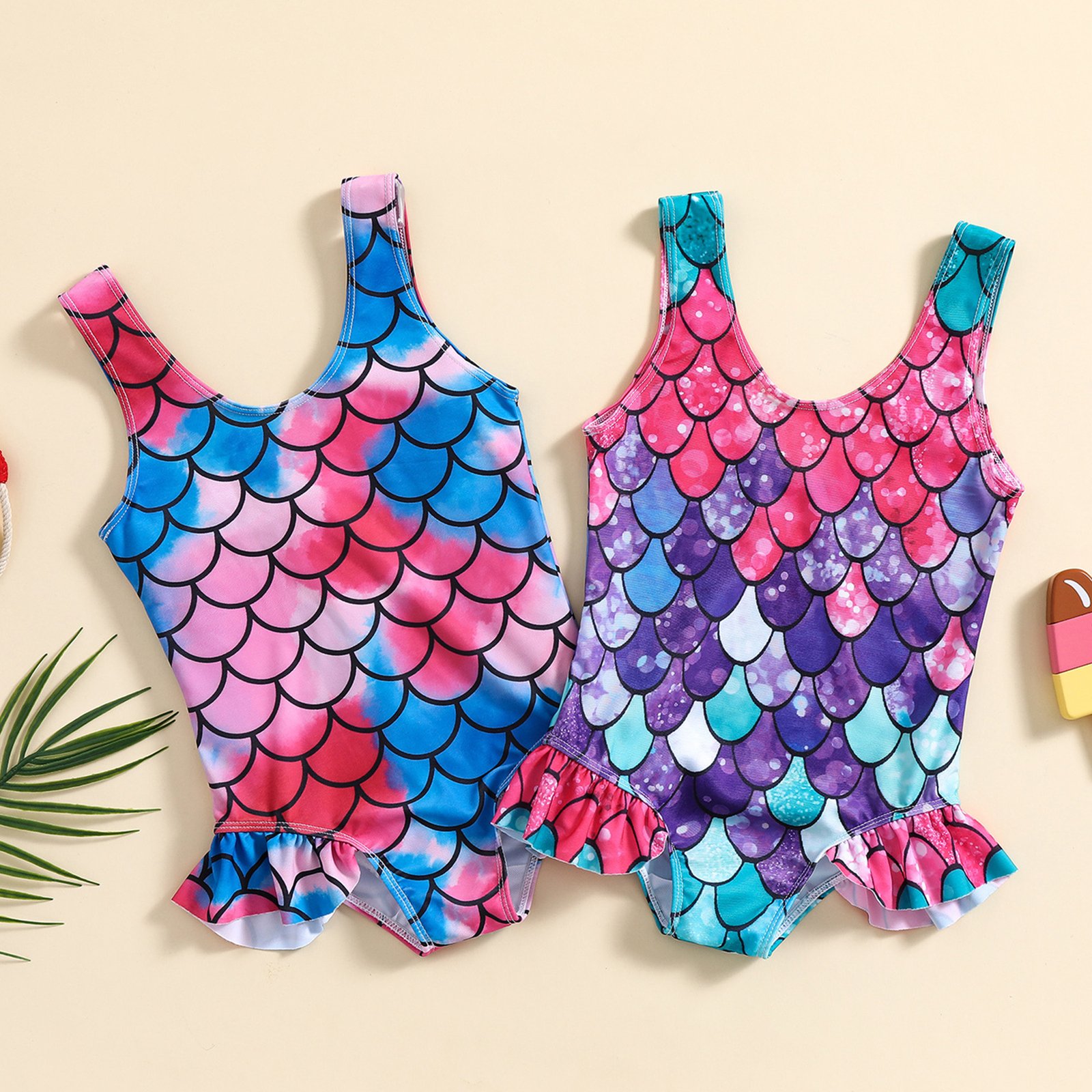Two girls' one-piece swimsuits featuring mermaid scale prints, wide shoulder straps, and ruffled hems.