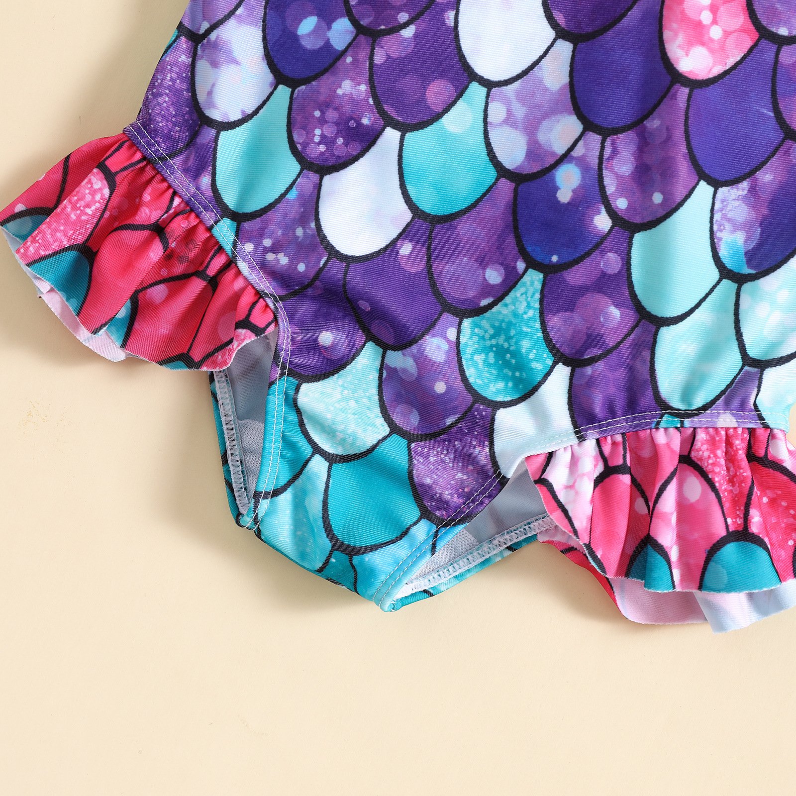 Close-up detail of a girls' mermaid scale print one-piece swimsuit featuring ruffled leg hems.