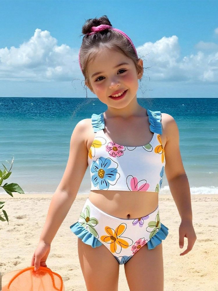 Girls' white floral print two-piece bikini set with ruffled blue straps and high-waisted ruffled bottoms.