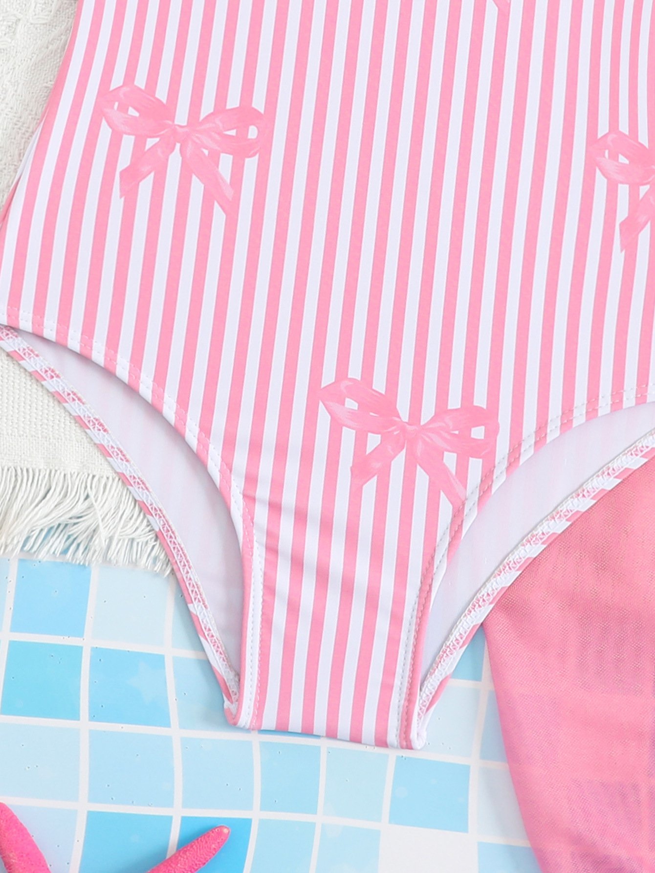 Close-up of a pink and white striped one-piece swimsuit bottom featuring bow prints and lace trim.