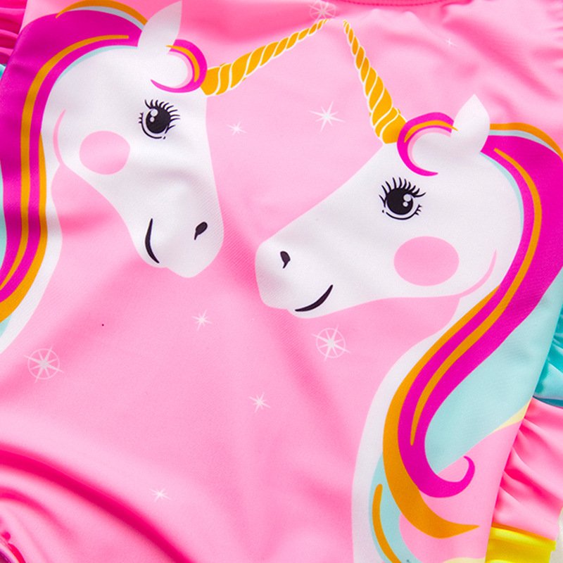 Close-up of a pink girls' one-piece swimsuit featuring a colorful unicorn print and ruffled side details.