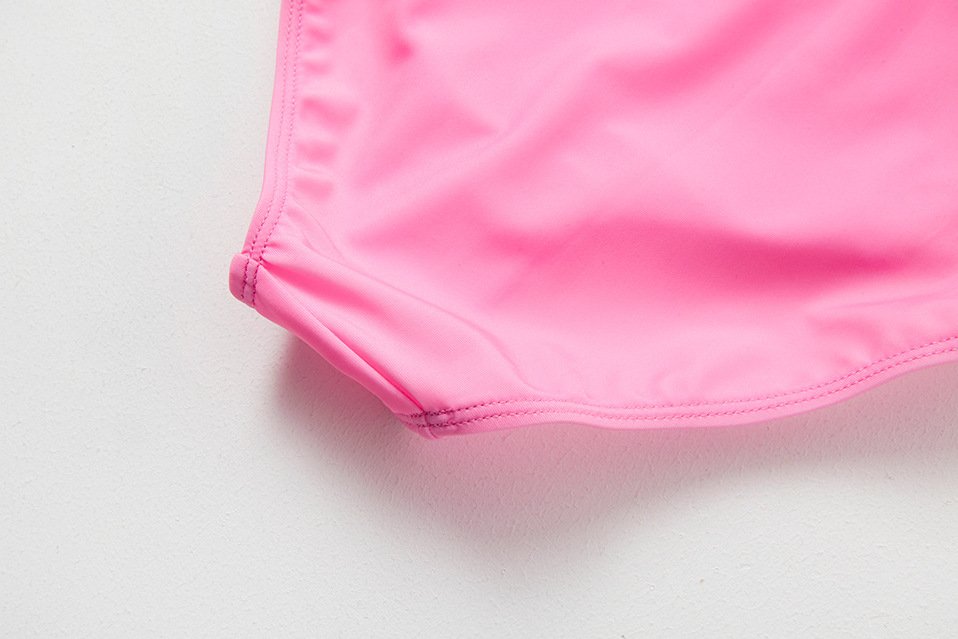 Close-up detail of a pink girls' one-piece swimsuit showing the bottom hem stitching and side panel construction.
