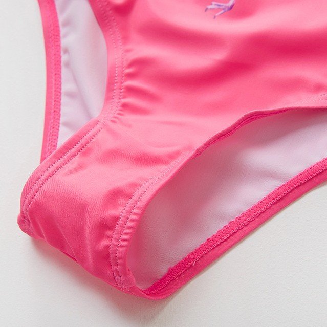 Close-up detail of a pink girls' one-piece swimsuit showing the leg opening, light pink lining, and stitching.