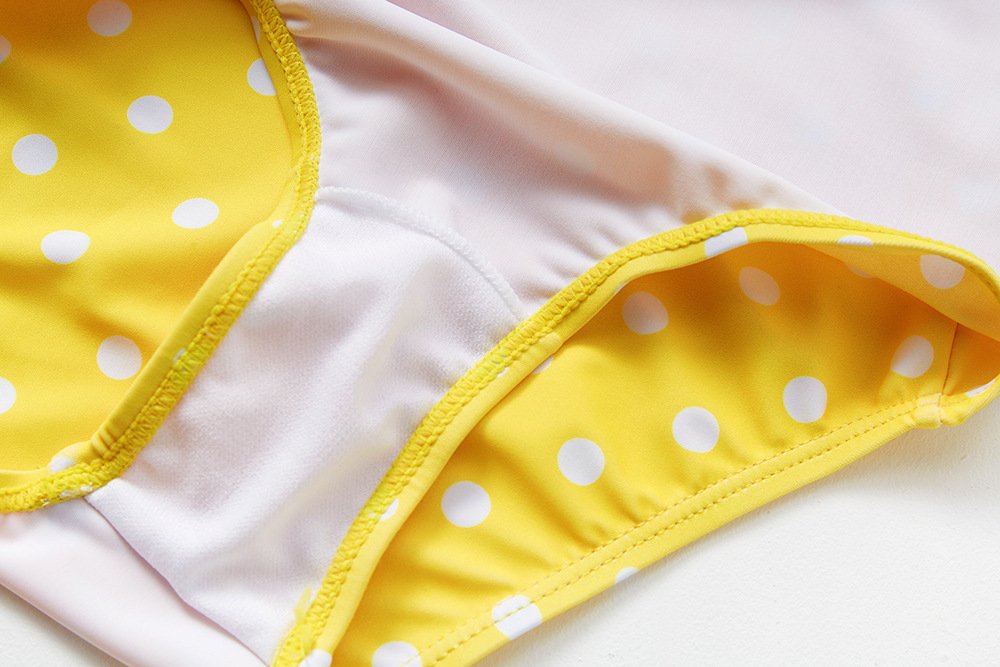 Close-up of yellow and white polka dot girls one-piece swimsuit with pink lining and yellow trim.