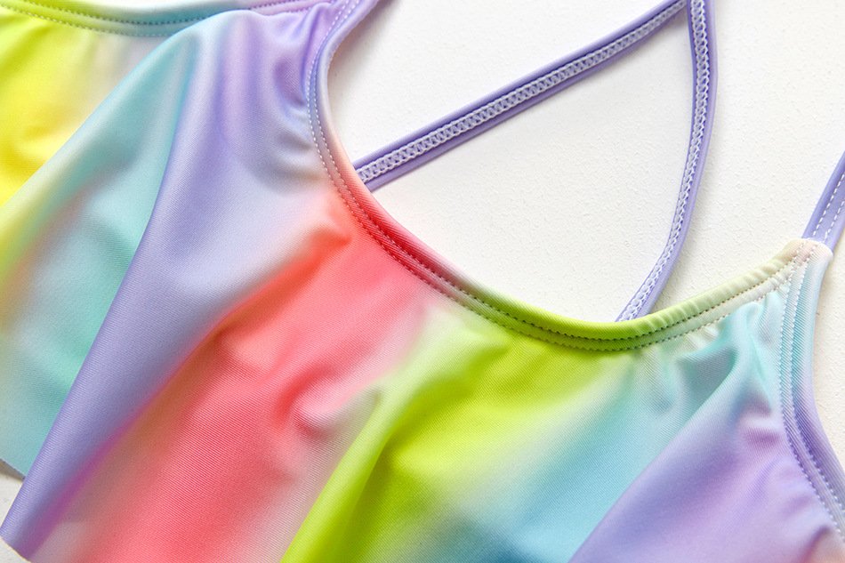 Close-up of a pastel rainbow tie-dye girls' tankini top with a scoop neckline and purple crossback straps.