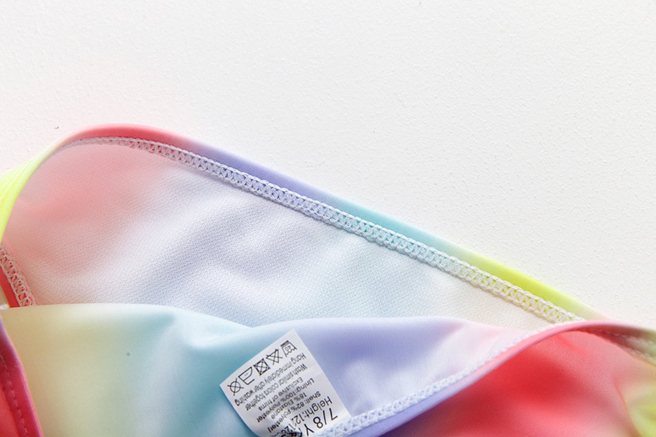 Close-up of a rainbow gradient girls' swimwear interior showing white lining, stitching, and a care label.