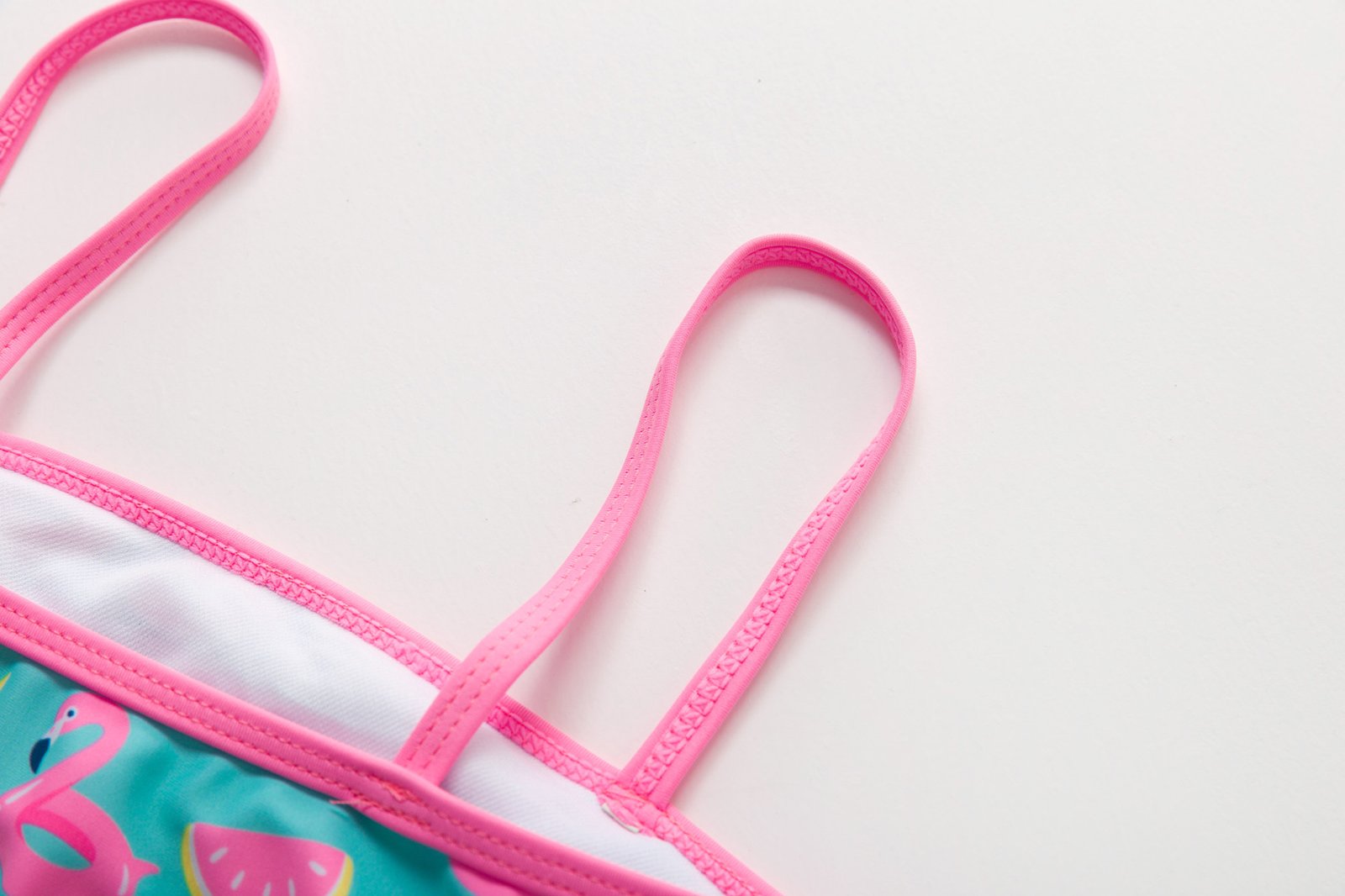 Close-up of a girls' bikini top with pink spaghetti straps, white lining, and flamingo print fabric.
