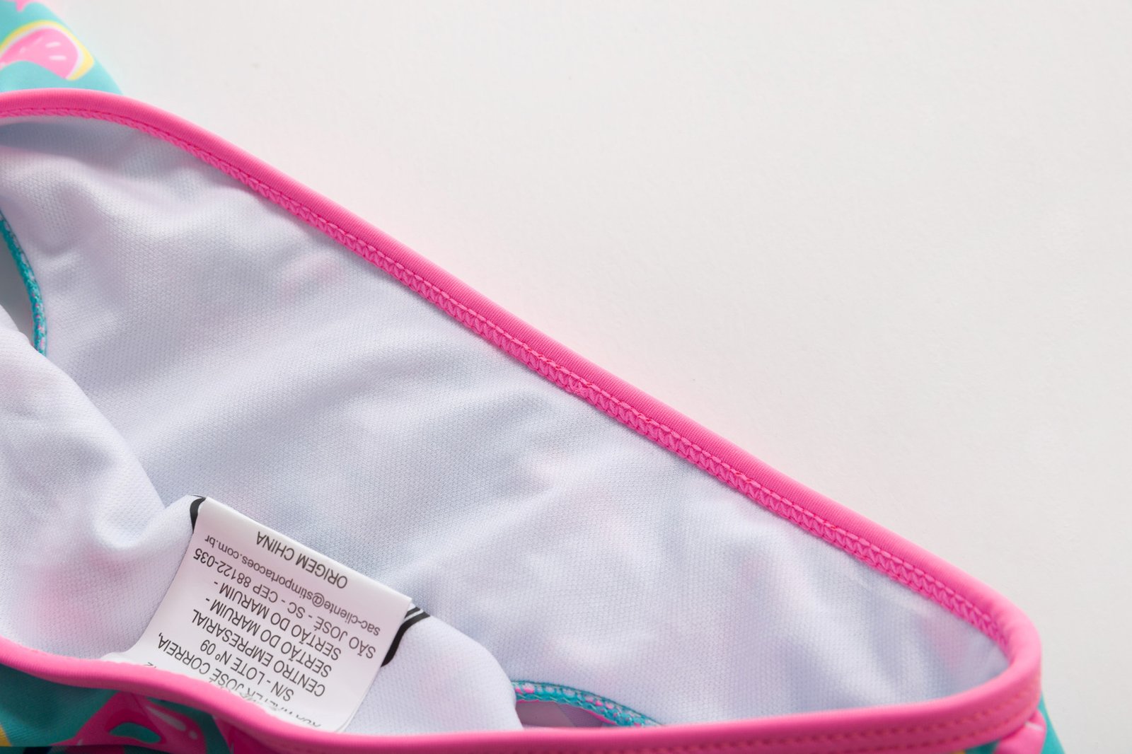 Close-up of white lined girls' bikini bottoms with pink trim and a visible care label.