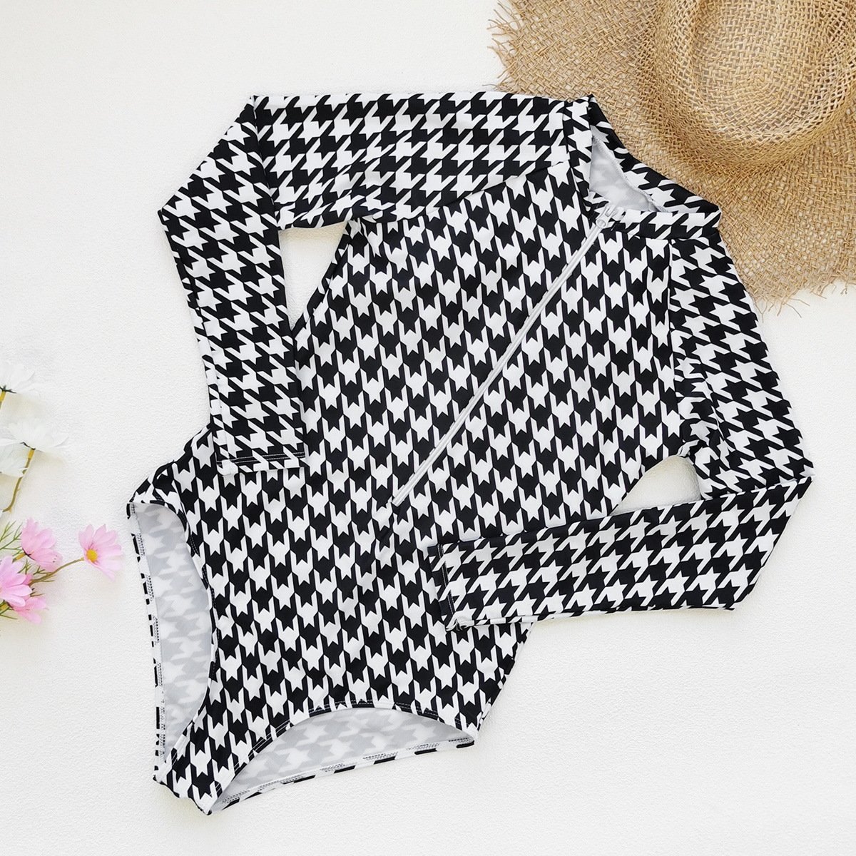 Black and white houndstooth long sleeve one-piece surf suit with diagonal front zipper and high-cut legs.