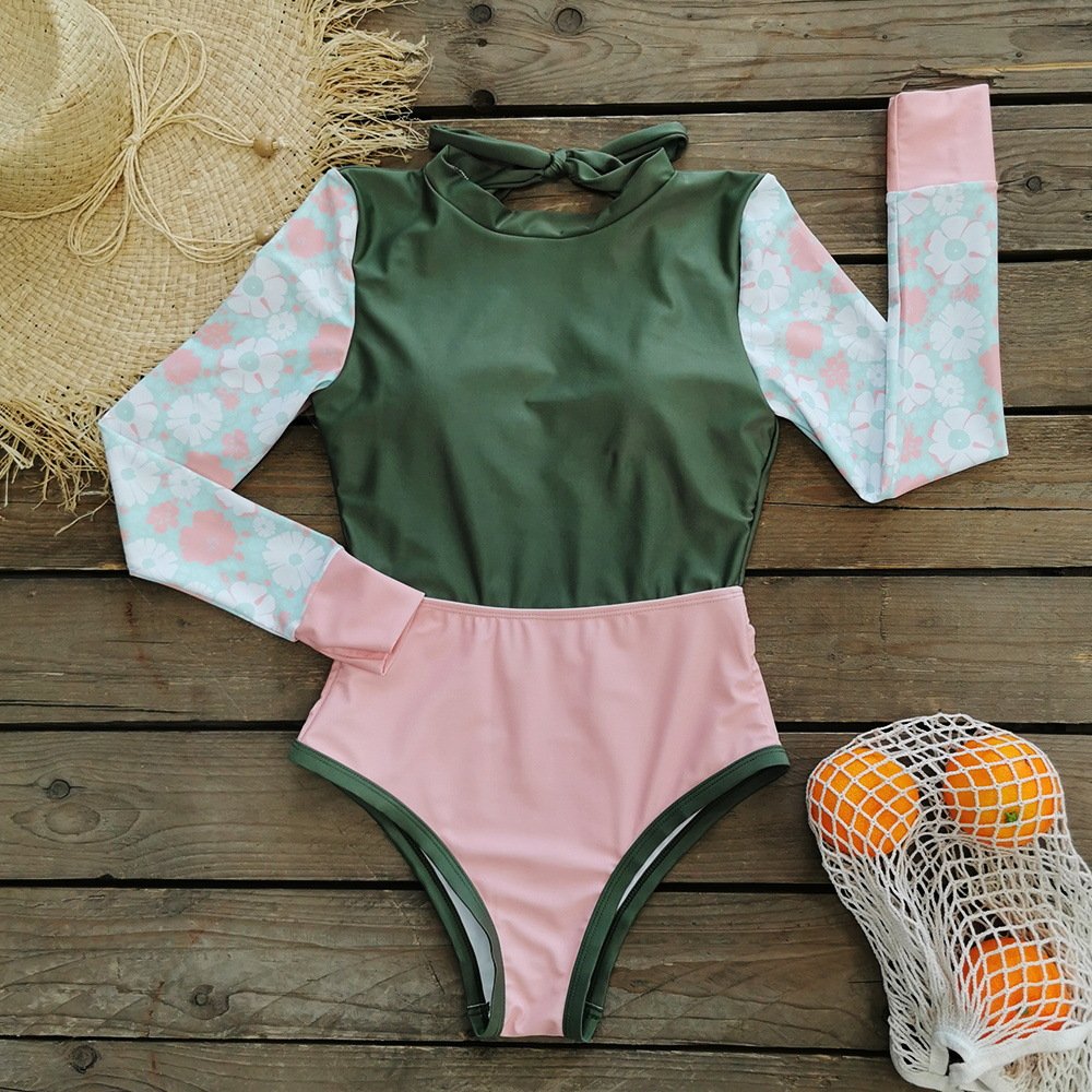 Long sleeve colorblock one-piece swimsuit featuring a green bodice, floral patterned sleeves, and a pink bottom with contrast