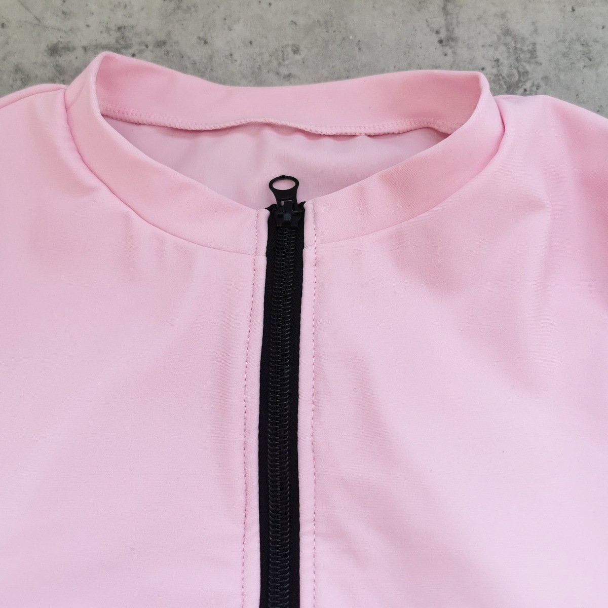 Close-up of a pink long-sleeve swimsuit featuring a stand collar and black front zipper.