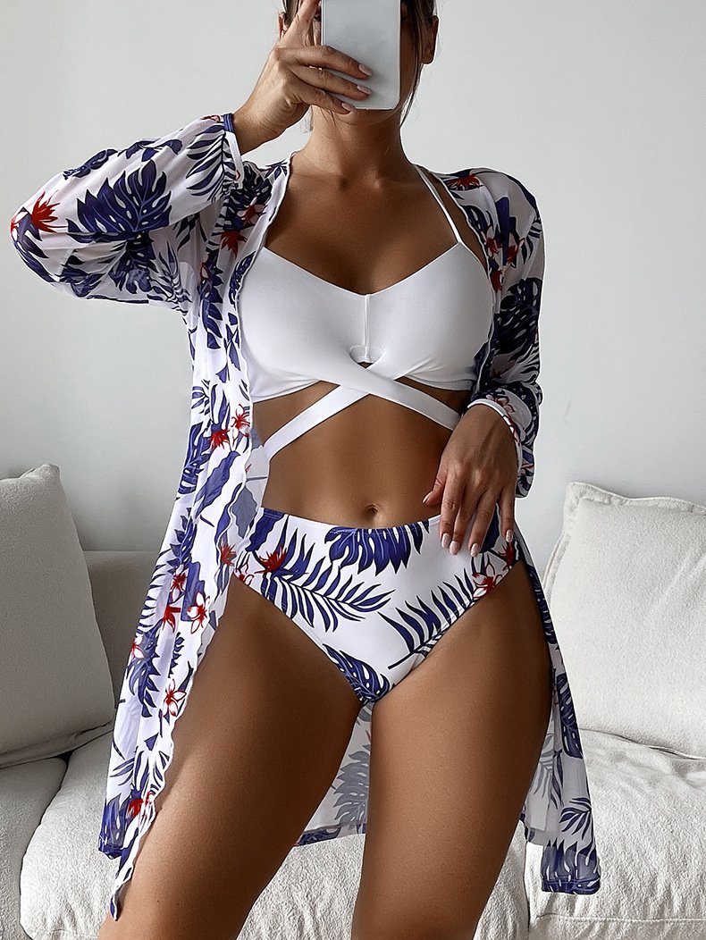 A three-piece bikini set featuring a white strappy cutout top, leaf-print high-waisted bottoms, and a matching long-sleeve open-front