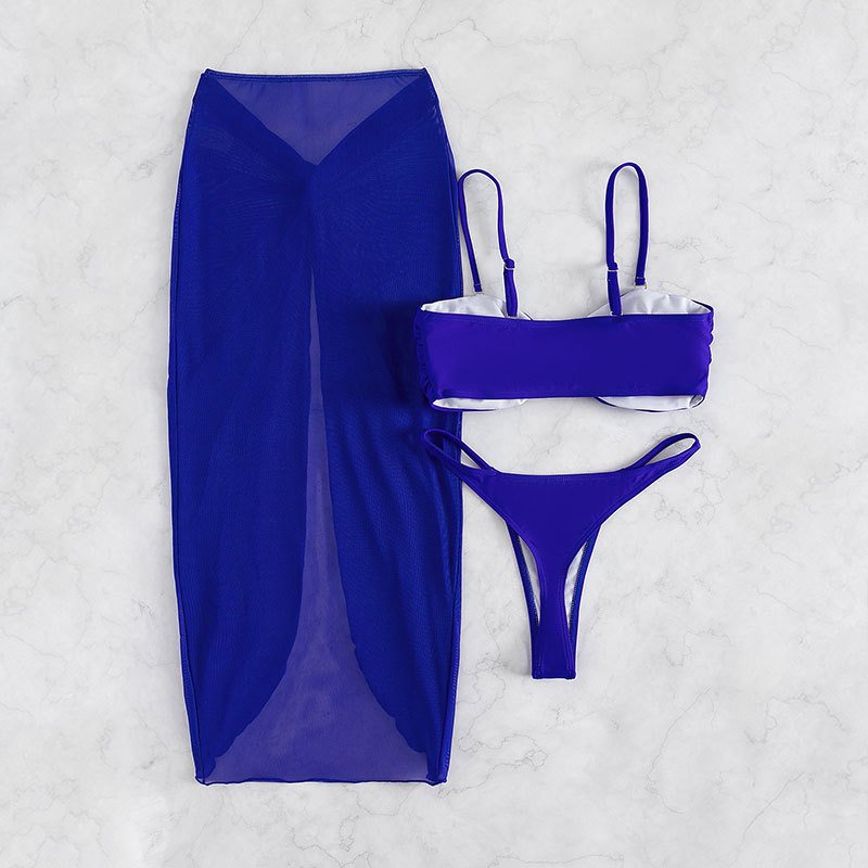 Blue three-piece swimwear set featuring a ruched bandeau top, thong bottoms, and a sheer high-waisted midi skirt cover-up.