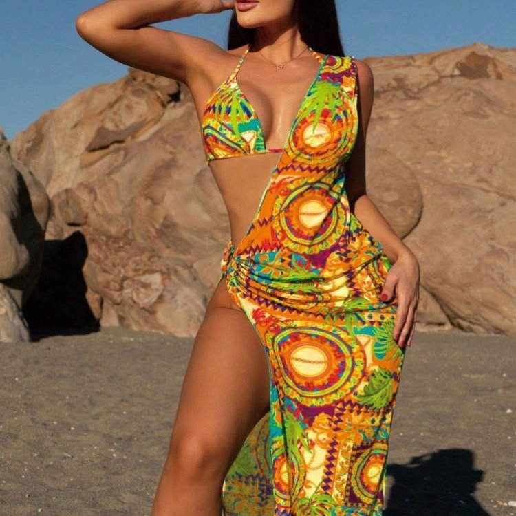 A woman wearing a colorful printed triangle bikini and a one-shoulder high-slit cover-up dress.