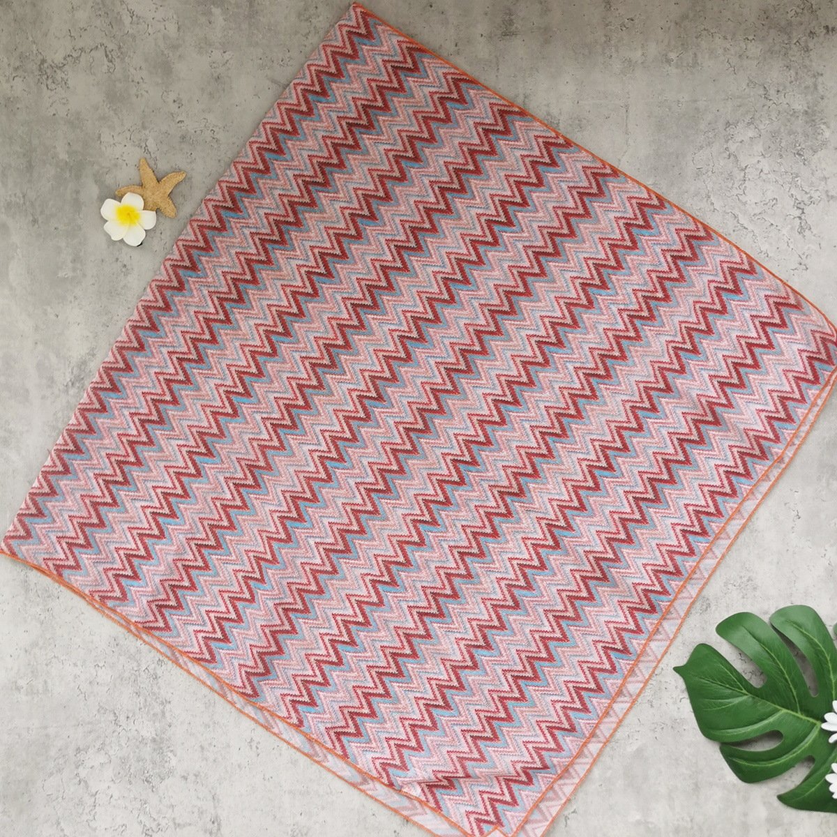 A rectangular beach towel featuring a colorful zigzag pattern in pink, blue, and red with an orange border.