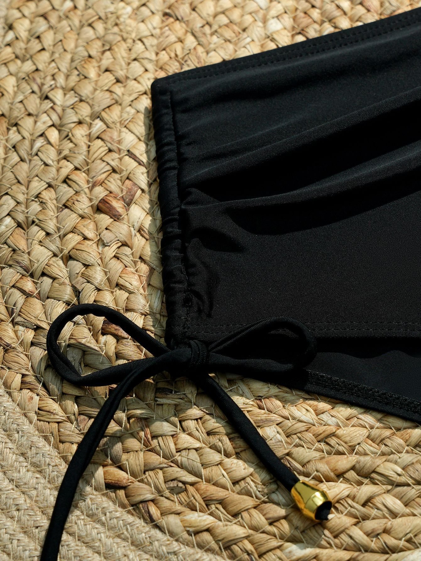 Close-up of a black high-waist bikini bottom featuring a ruched front panel and adjustable side tie with a