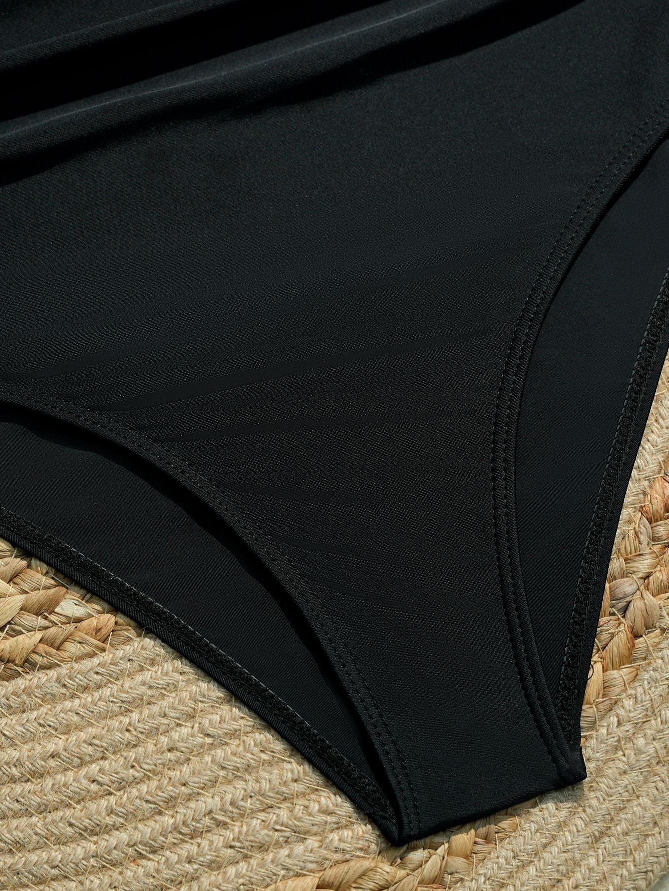 Close-up detail of black high-waist bikini bottoms with side tie straps on a woven mat.