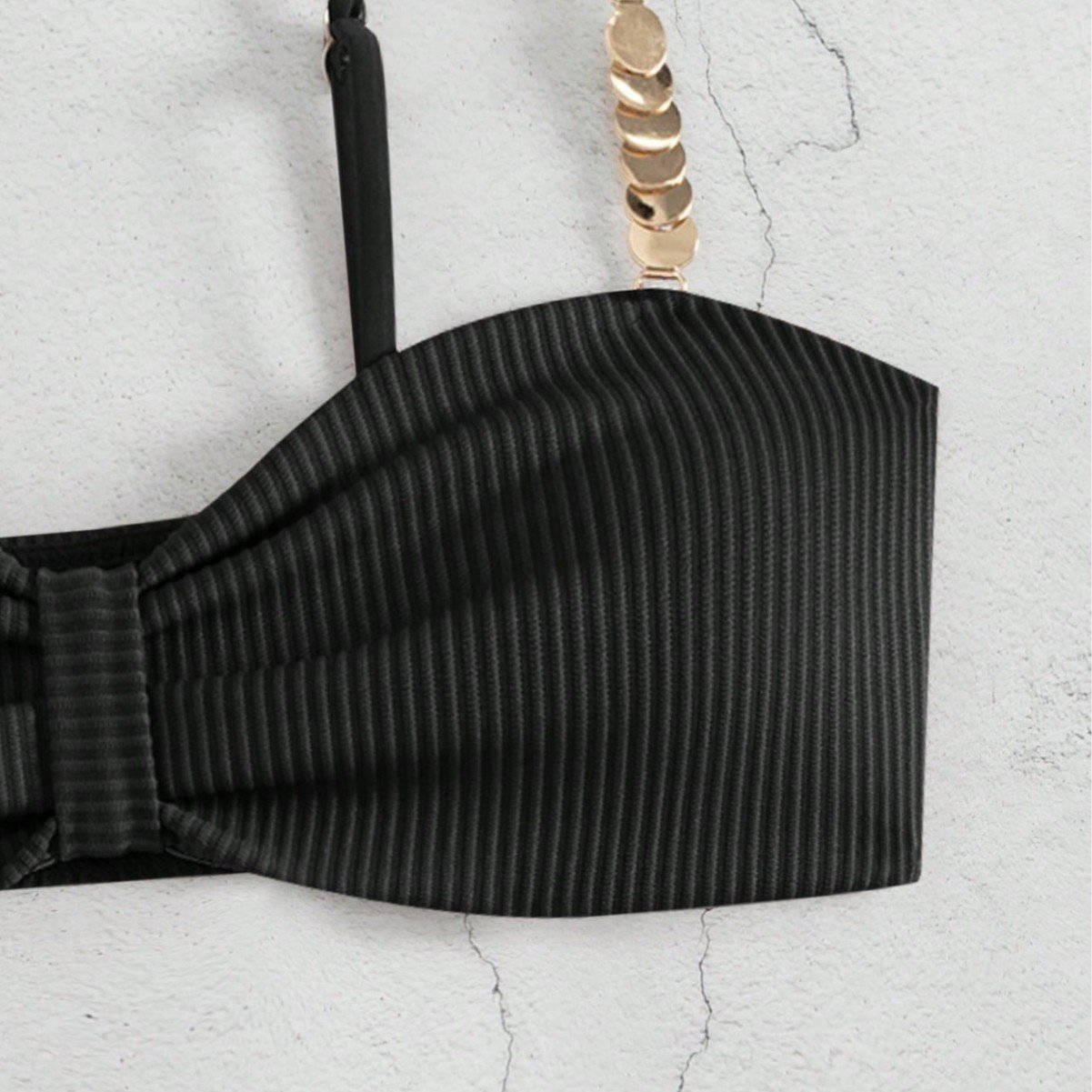 Close-up of a black ribbed bandeau bikini top featuring a center twist and gold chain strap detail.