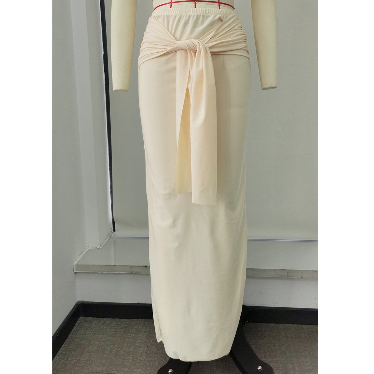 Cream long maxi skirt with a front knot tie detail and elastic waistband on a mannequin.