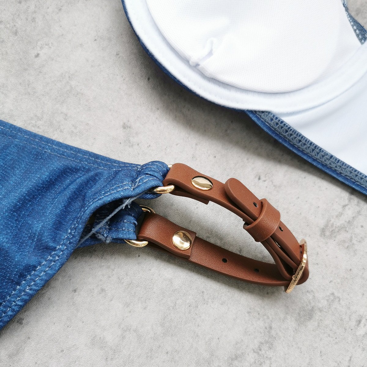 Close-up of blue denim bikini bottom side strap with brown leather buckle detail and white underwire top.