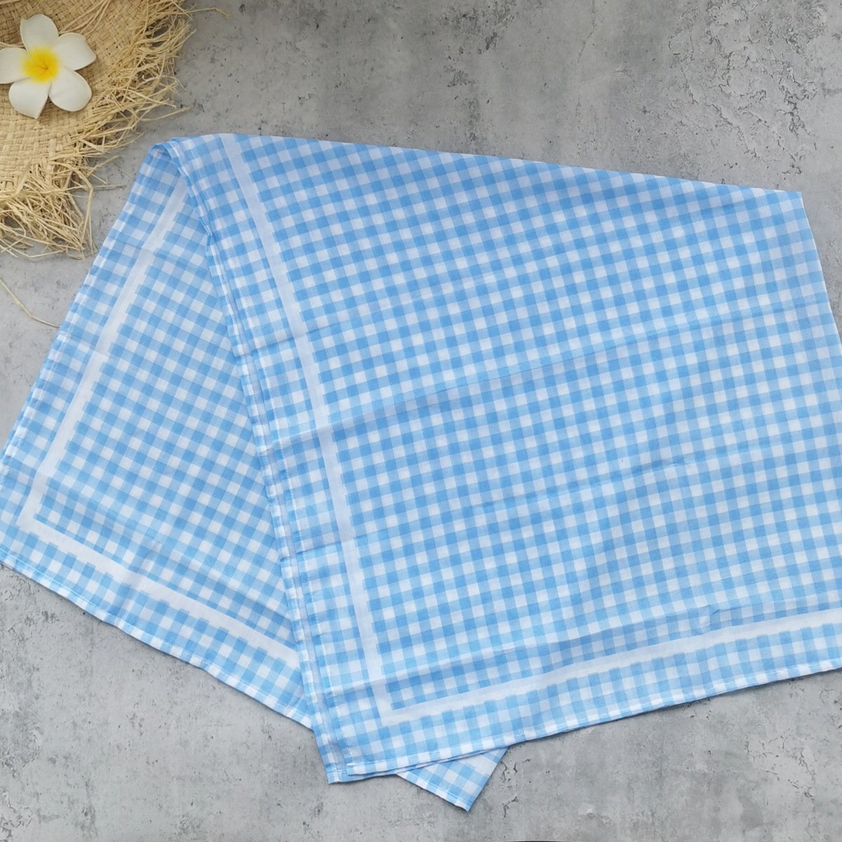 Blue and white gingham check fabric folded flat on a concrete surface.