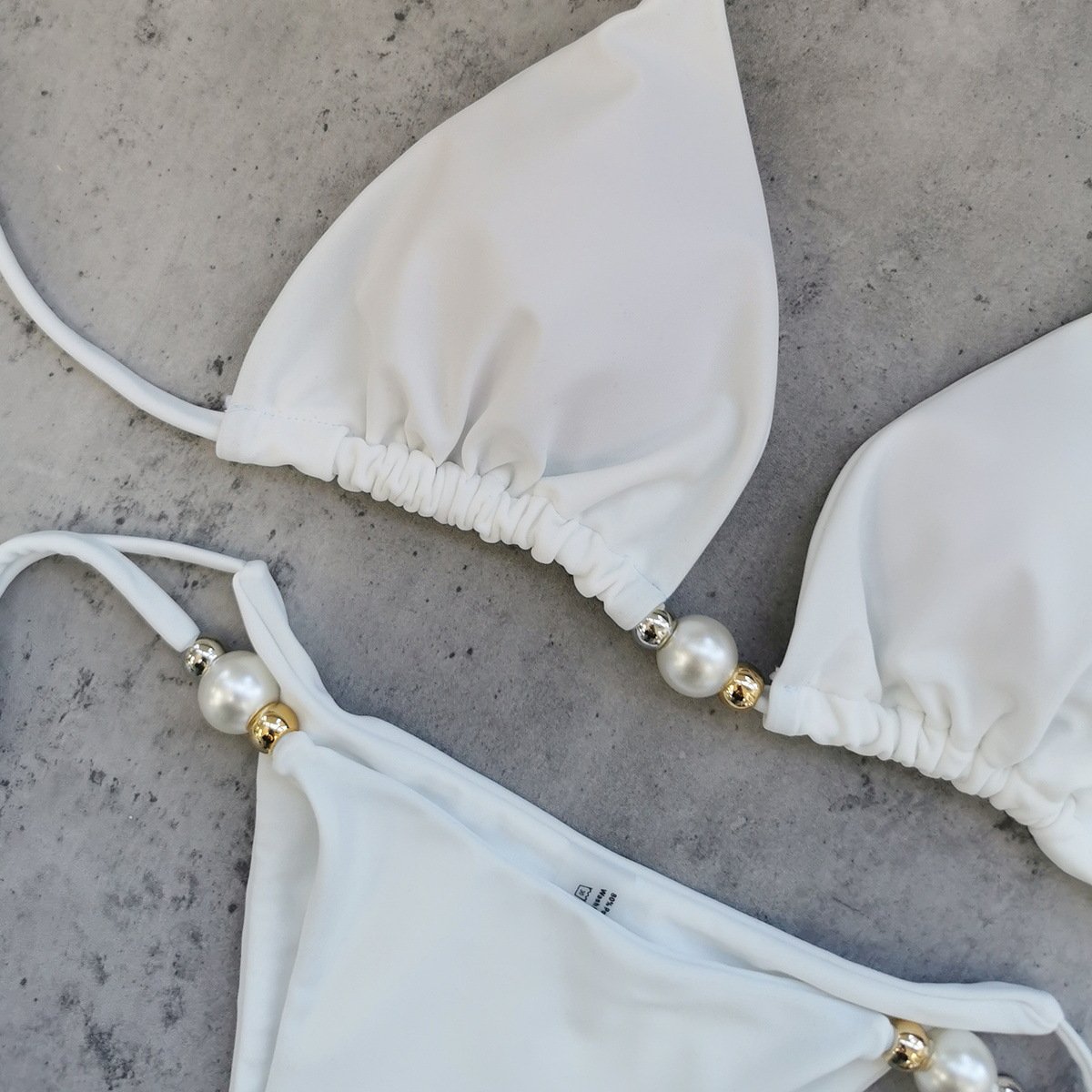White two-piece bikini set featuring a gathered triangle top and high-cut bottoms with pearl and bead accents.