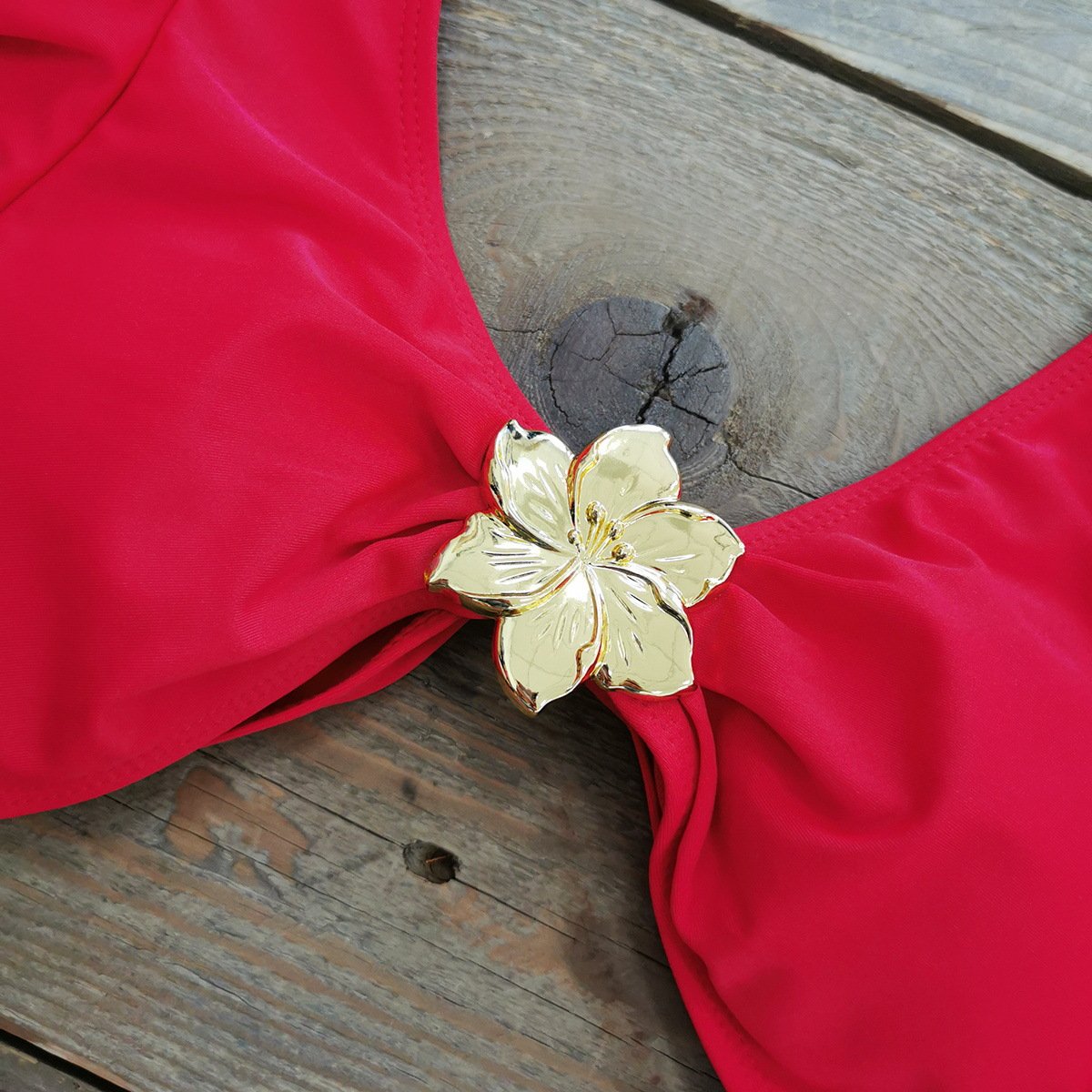 Close-up of a red bikini top featuring a plunging V-neckline and a gold metal flower detail at the