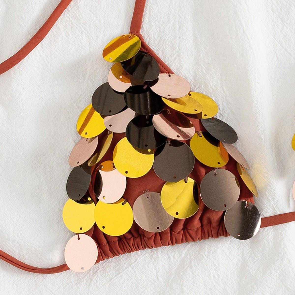 Close-up of a rust-colored triangle bikini top covered in overlapping gold, silver, and rose gold sequins with a