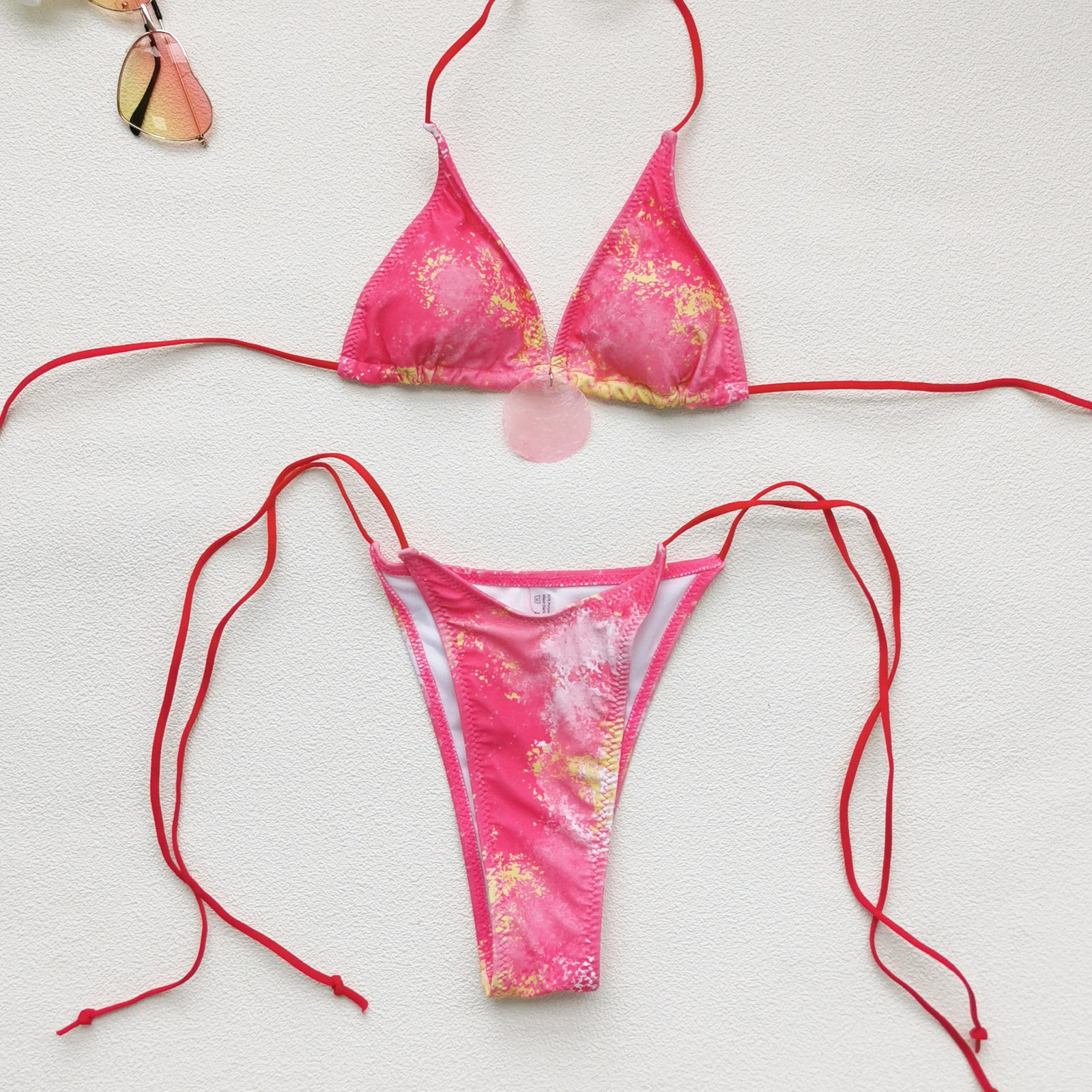 Pink and yellow tie-dye triangle bikini set with red string straps and center pendant detail.