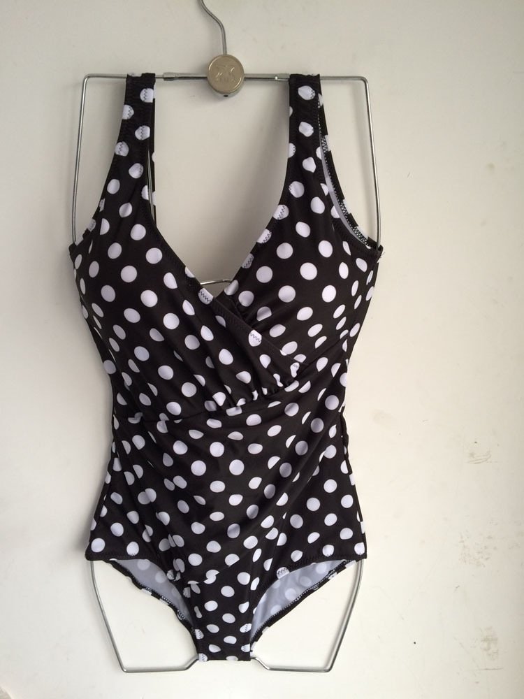Black and white polka dot one-piece swimsuit featuring a wrap-front V-neckline and wide shoulder straps.