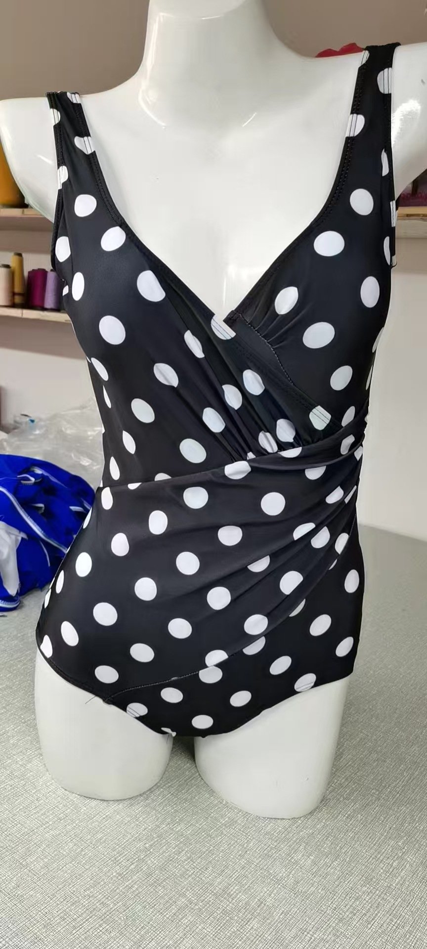 Black and white polka dot one-piece swimsuit featuring a deep V-neck wrap front and wide straps.