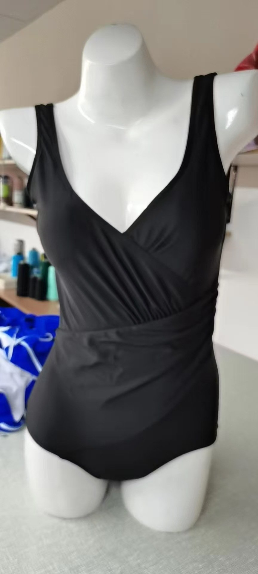 Black one-piece swimsuit with a deep V-neckline, wrap-front bodice, and wide shoulder straps.