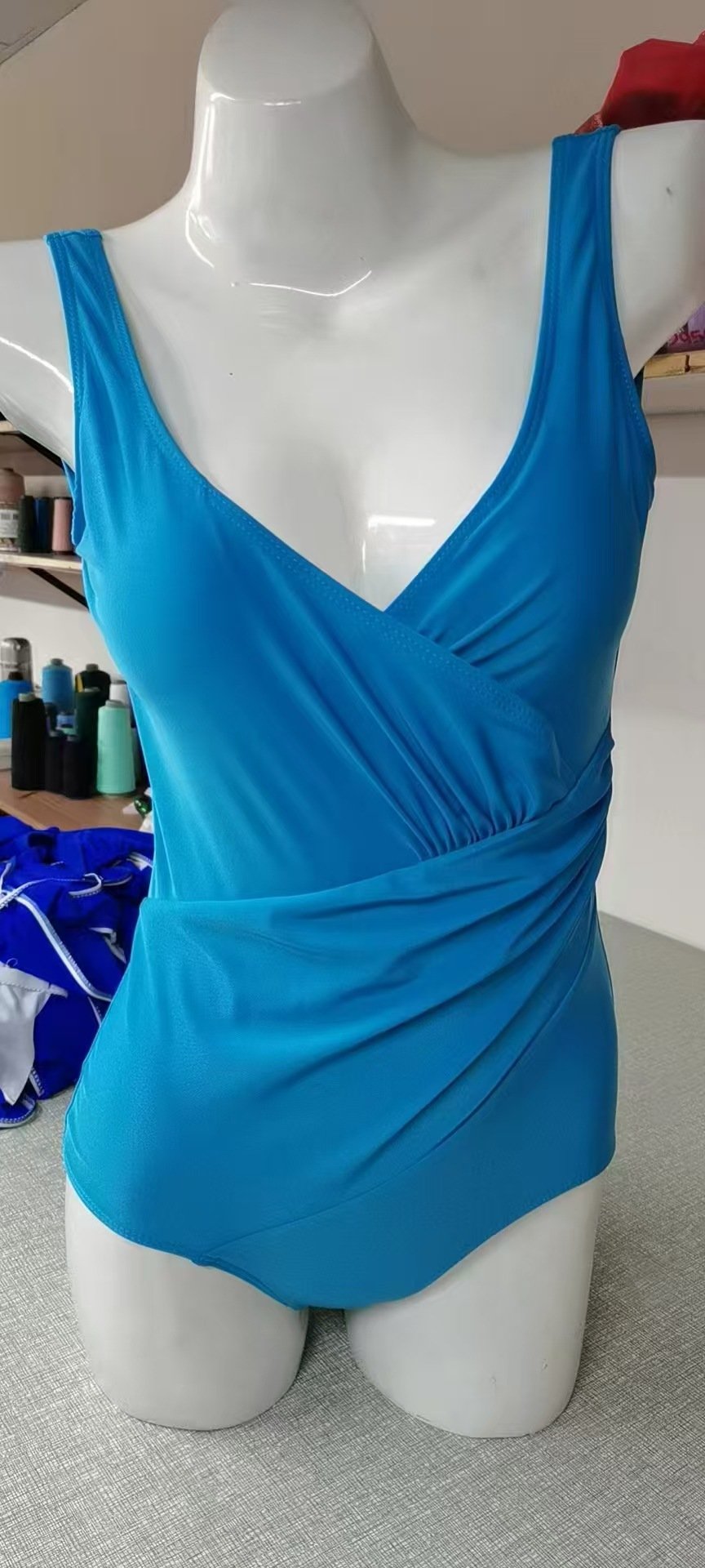 Blue one-piece swimsuit featuring a deep V-neckline, wrap-front bodice, and wide shoulder straps.