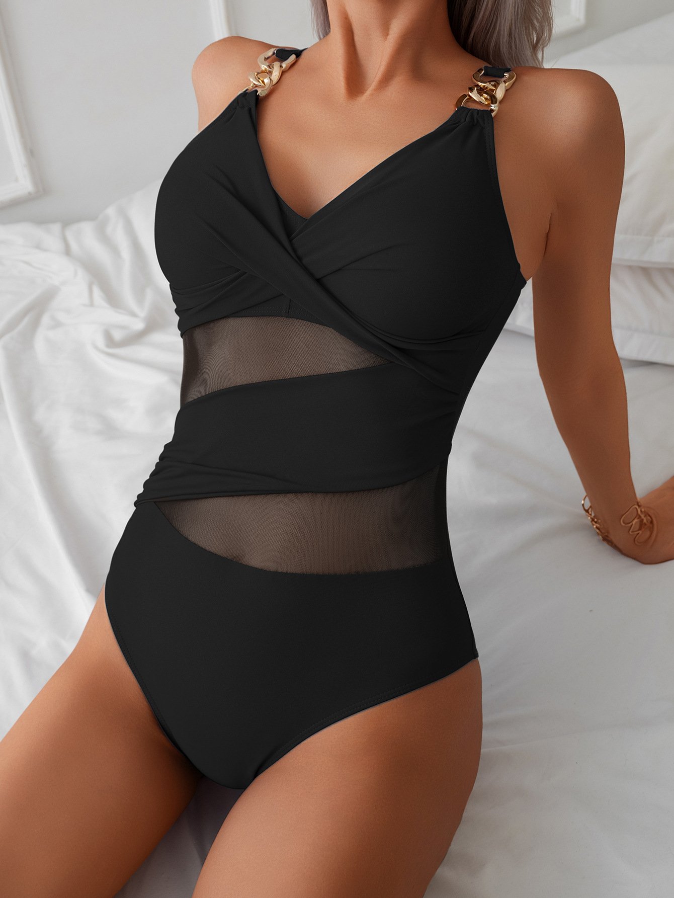 Black one-piece swimsuit with gold chain straps, V-neck crisscross bodice, and sheer mesh waist panels.