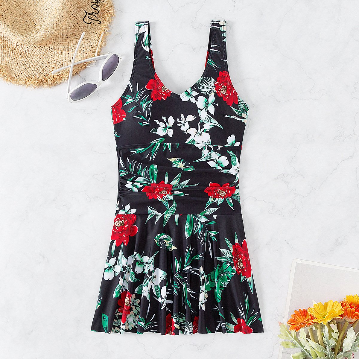 Black floral print sleeveless one-piece swimsuit with a V-neckline and flared skirt overlay.