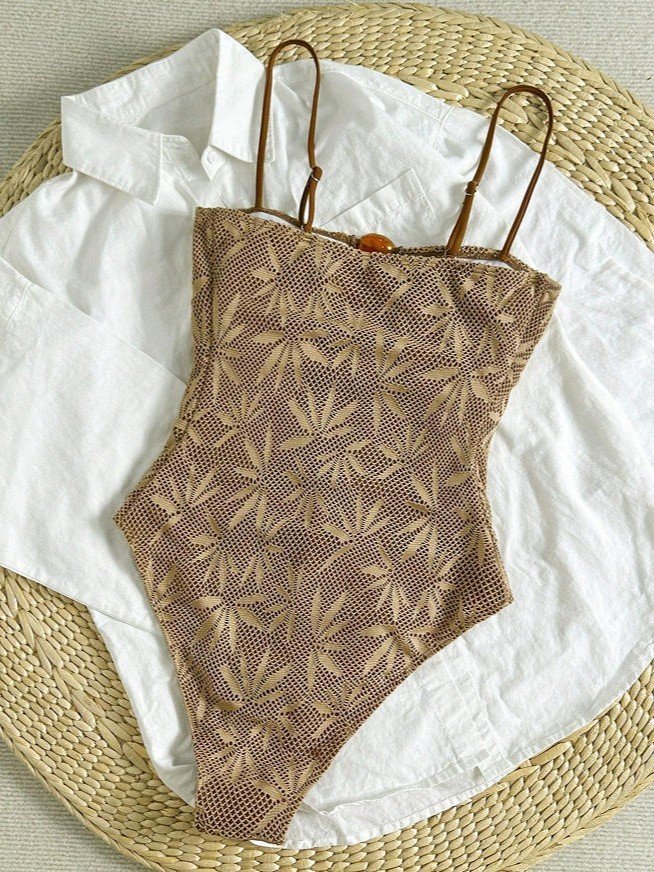 Brown and beige leaf print one-piece swimsuit with adjustable spaghetti straps and button closure.