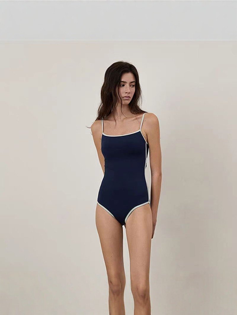 Model wearing a navy blue one-piece swimsuit with white contrast trim and thin spaghetti straps.