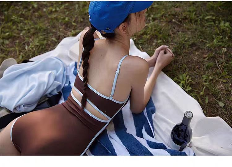 Brown one-piece swimsuit with light blue contrast trim, featuring adjustable spaghetti straps and a strappy open back design.